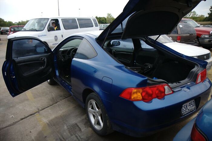 Blue car parked with doors and trunk open in lot, illustrating startling windshield notes found by online community members.