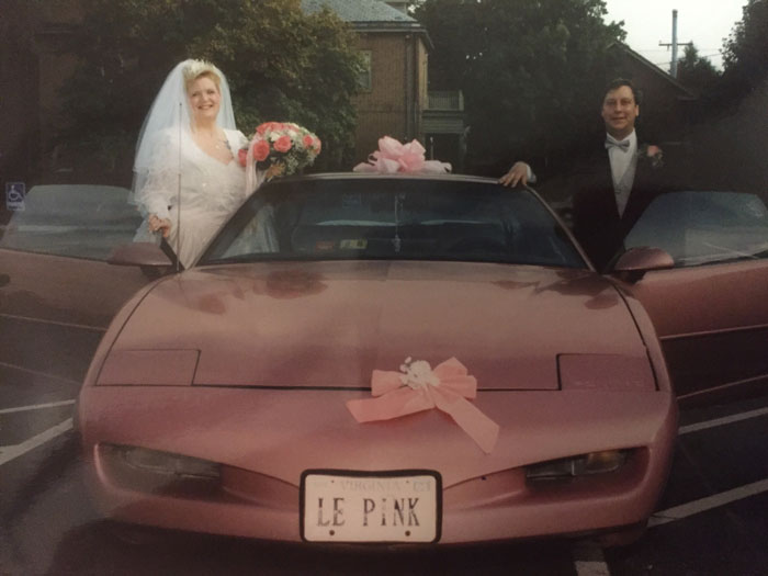Bride and groom standing beside a pink car with a windshield, highlighting startling windshield notes found by folks.