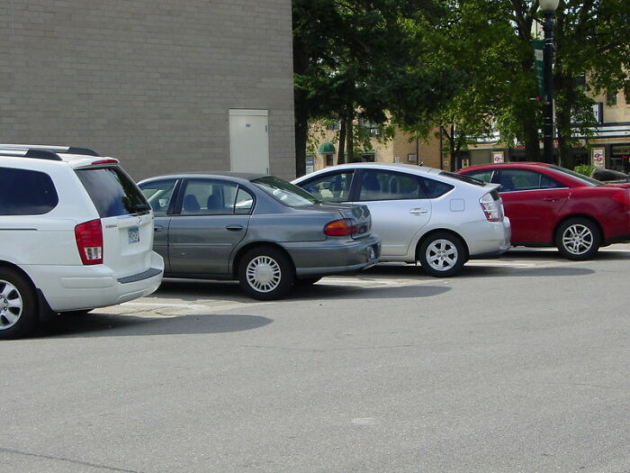 Several cars parked in a lot with a windshield note visible on the gray sedan, highlighting startling windshield notes.