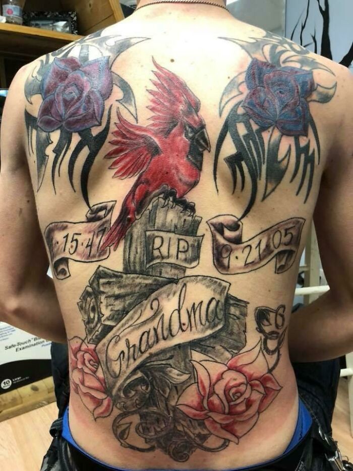 Crucifix with roses, a cardinal, and "Grandma" tattoo, showcasing a bold, intricate back piece design.