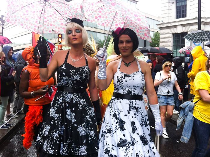 People in floral dresses and holding umbrellas at LGBTQ+ pride event.