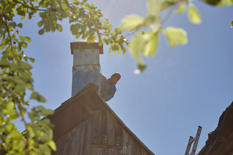 The Painter-Climber Paints The Chimney. A Worker On A Blue Sky Background.