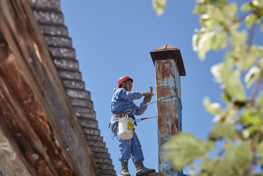 The Painter-Climber Paints The Chimney. A Worker On A Blue Sky Background.
