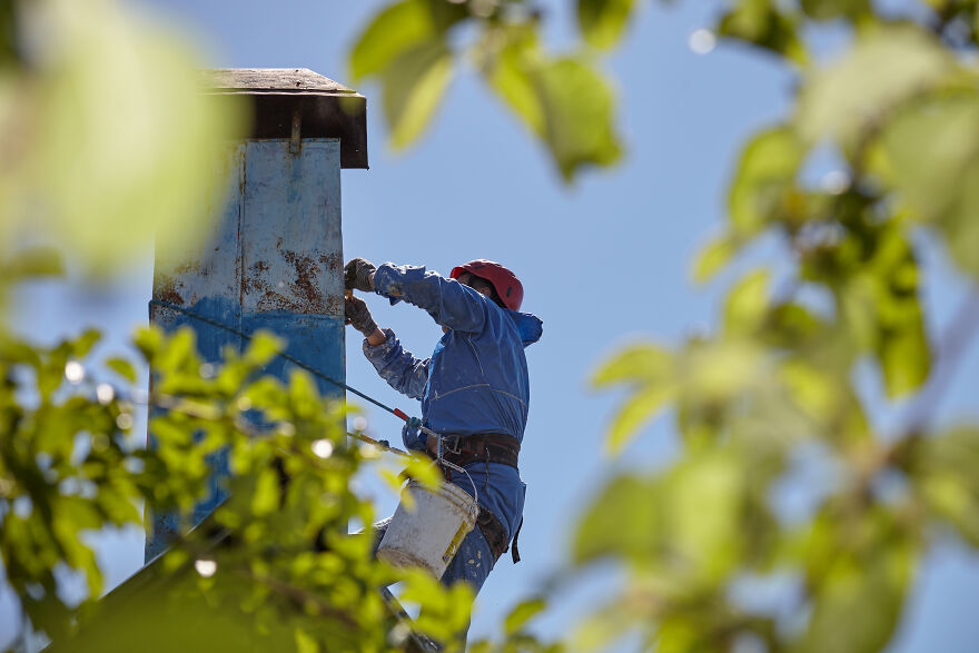 The Painter-Climber Paints The Chimney. A Worker On A Blue Sky Background.