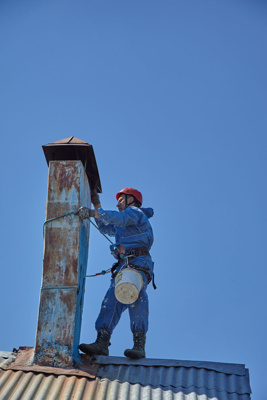 The Painter-Climber Paints The Chimney. A Worker On A Blue Sky Background.