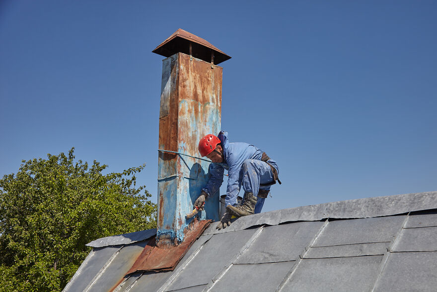 The Painter-Climber Paints The Chimney. A Worker On A Blue Sky Background.