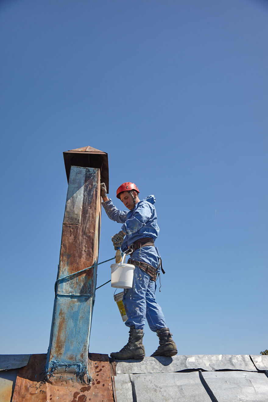 The Painter-Climber Paints The Chimney. A Worker On A Blue Sky Background.
