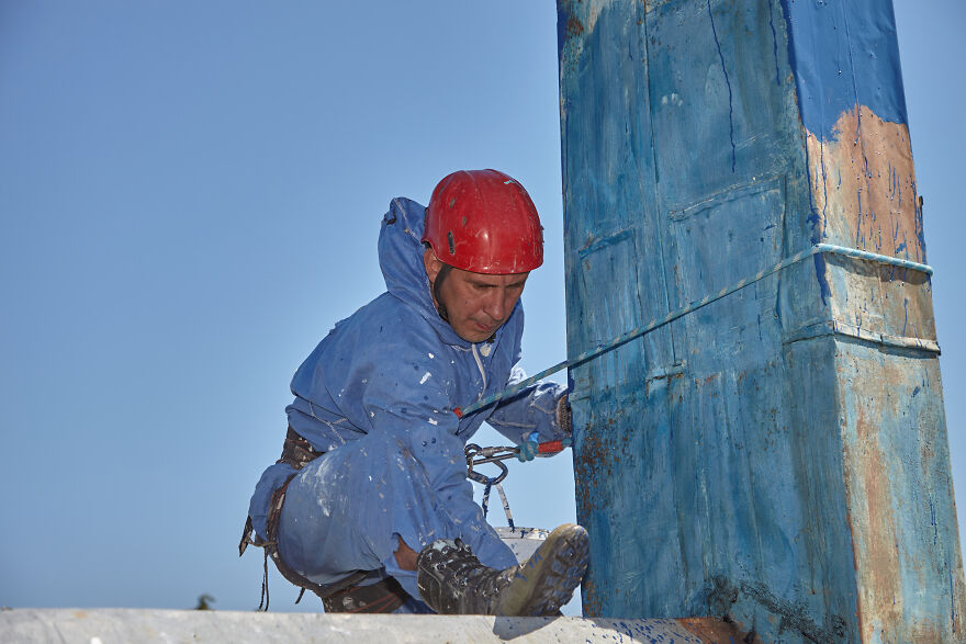 The Painter-Climber Paints The Chimney. A Worker On A Blue Sky Background.