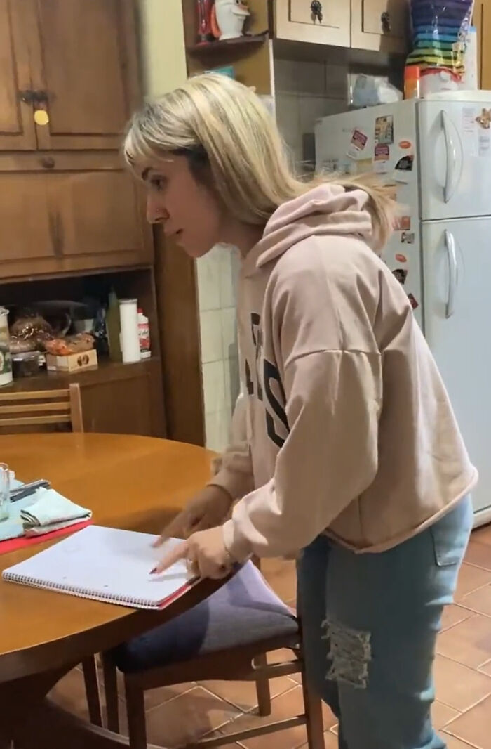 Girl in a kitchen pointing at a notebook, associated with grandparents' emotional tattoo reaction.