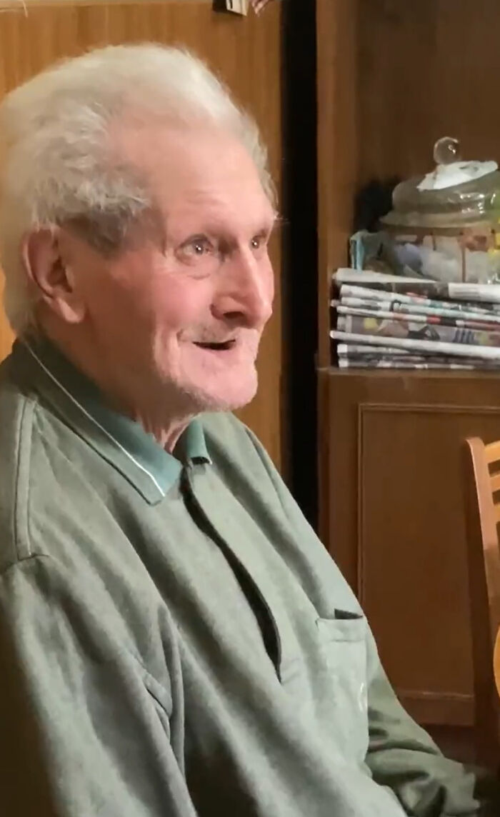 Grandfather's emotional reaction, smiling warmly while seated in a cozy room setting.