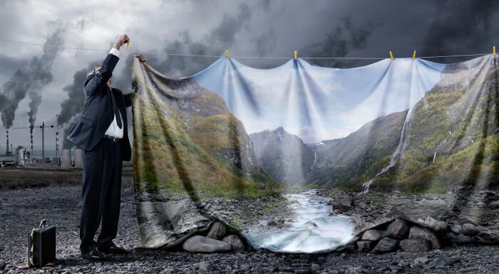 Man hanging a large vivid landscape photo backdrop in a polluted industrial area, illustrating powerful photography.