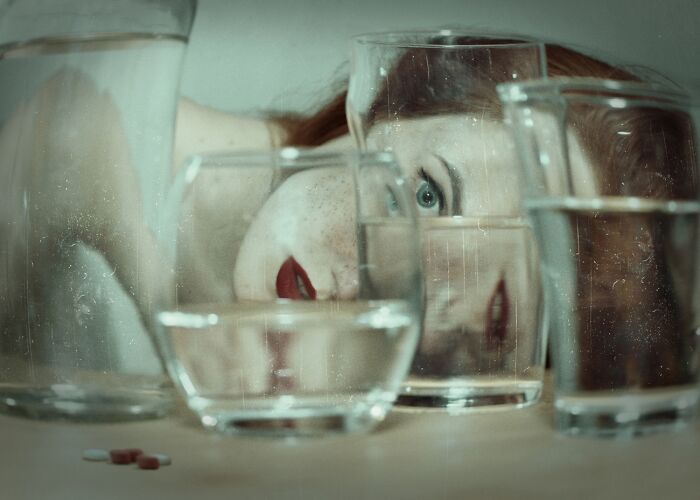 Woman with red lipstick and freckles seen through multiple glass cups filled with water, showcasing powerful photography techniques.