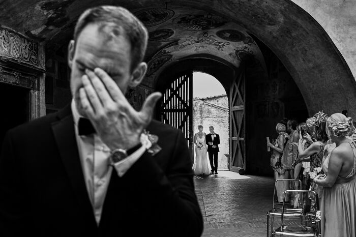 Black and white powerful photography capturing a groom wiping tears as bride walks down the aisle, Siena International Photo Awards style.