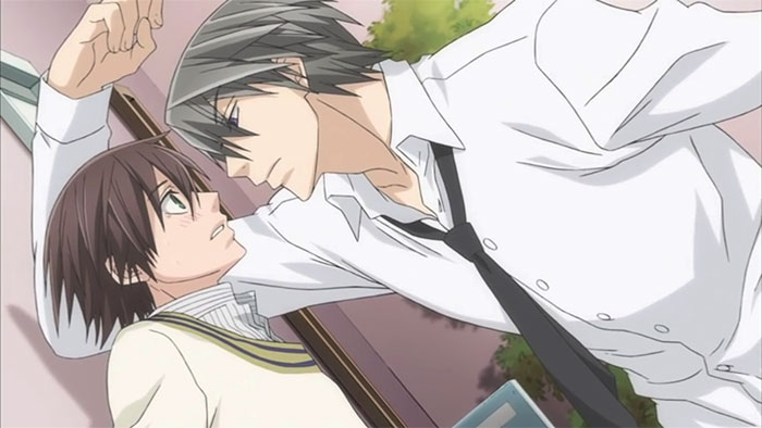 Anime couple in romantic scene, one leaning against a wall, creating tension and closeness.