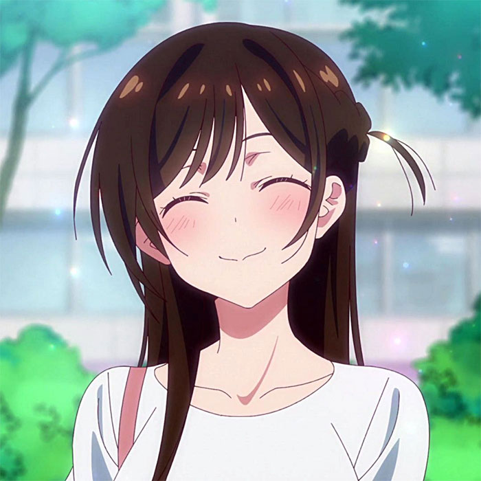 Smiling female anime character with long brown hair and white shirt, outdoors with blurred green background.