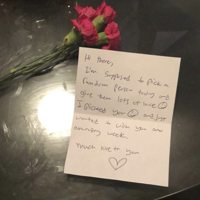 Handwritten windshield note with a kind message alongside red flowers, one of the most startling windshield notes found.