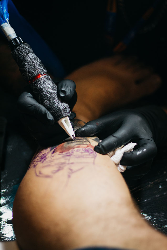 Tattoo artist with gloves working on a client's arm, illustrating professional tattooing.