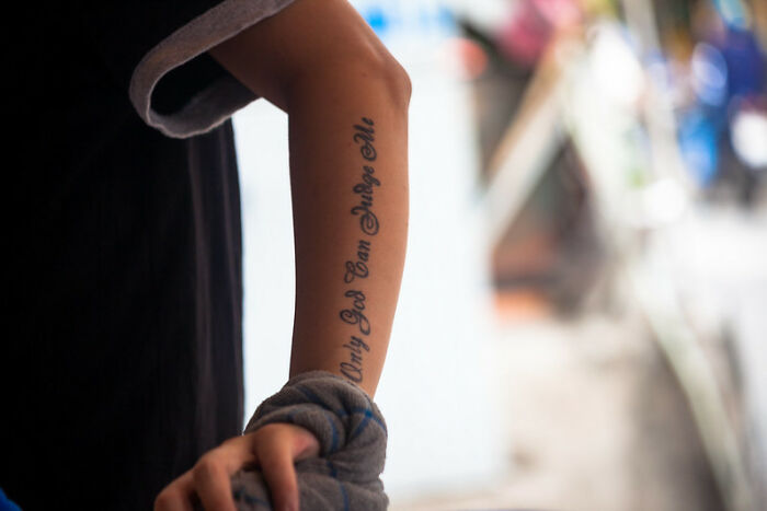 Forearm tattoo with "Only God Can Judge Me" text, often discussed as a red flag by people.