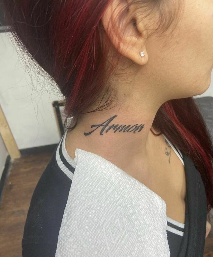 Neck tattoo script on woman's side neck in a hair salon, potential red flag tattoo.