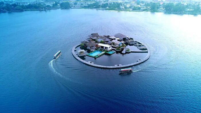 Bizarre buildings on a circular man-made island surrounded by water with boats nearby in a unique architectural setting.