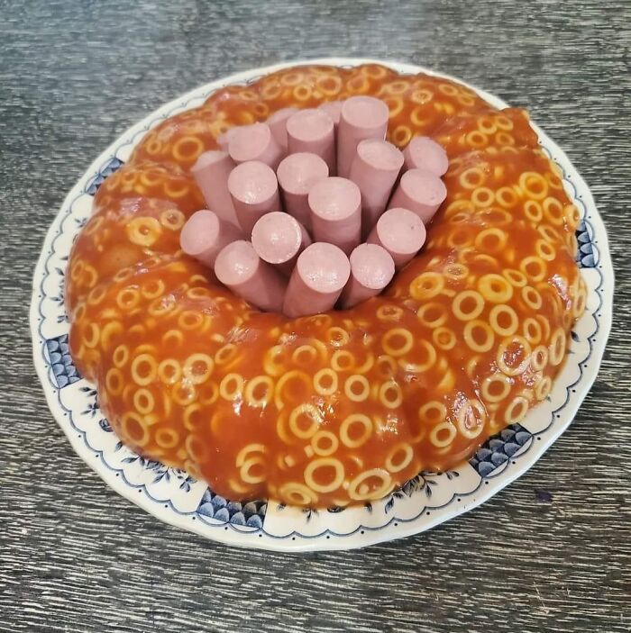 Unappetizing food with threatening auras showing hot dogs embedded in a gelatin mold filled with spaghetti rings in tomato sauce.