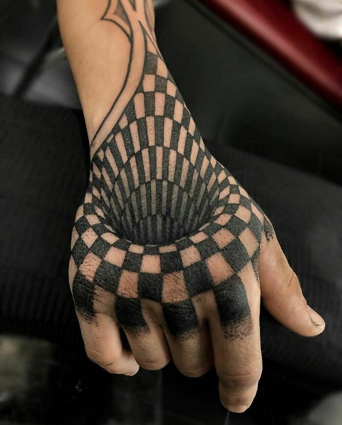 Hand with a 3D illusion tattoo creating a checkered vortex effect.