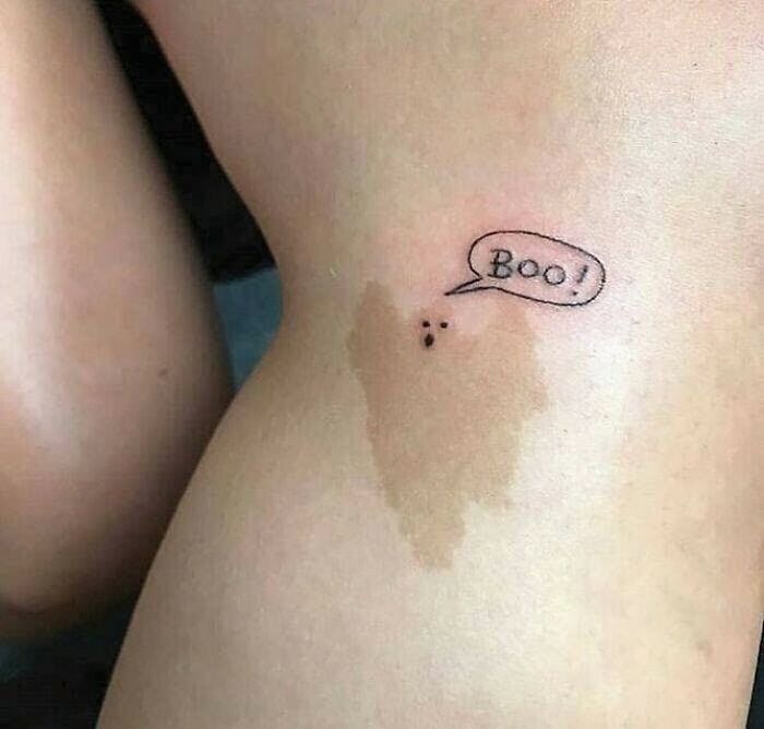 Crazy tattoo design of a playful ghost with "Boo!" speech bubble on skin.