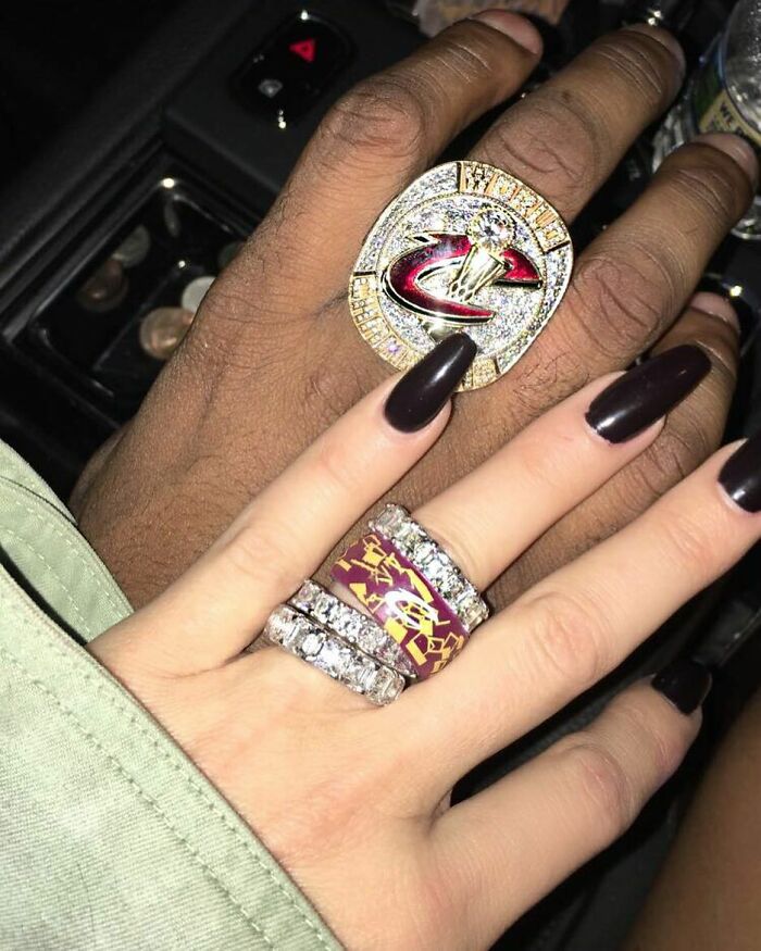 Two hands displaying large, extravagant rings, highlighting celebrity wealth with luxurious jewelry in a car setting.