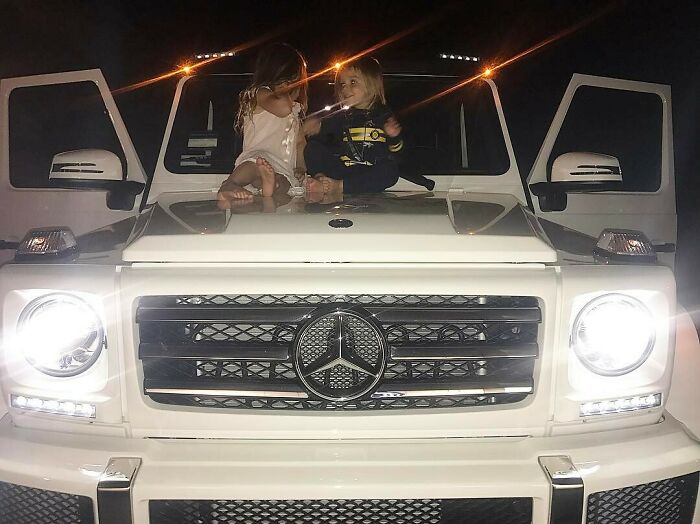 Children sitting on a luxury Mercedes SUV, highlighting celebrity wealth.