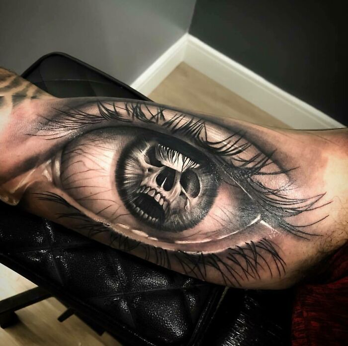 Close-up of a tattoo featuring a realistic eye with a skull pupil, showcasing a crazy tattoo design.