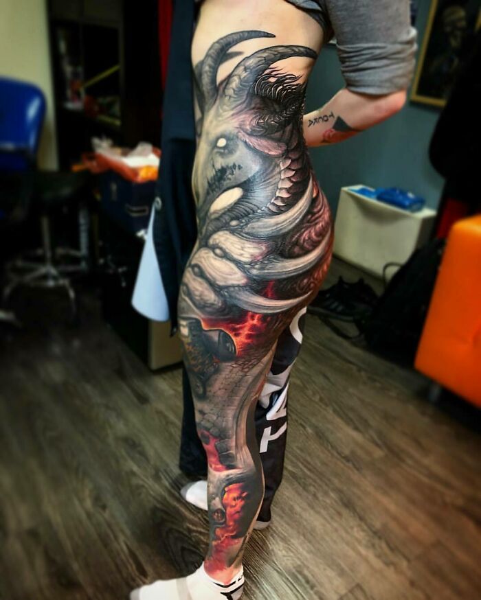 Person displaying a detailed, colorful tattoo covering their side and leg on wooden floor background.