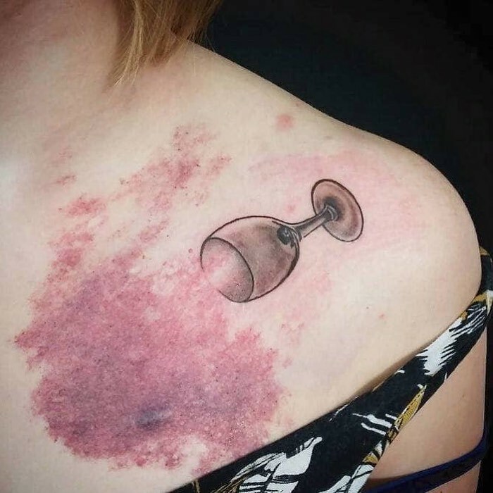 Tattoo of a tilted wine glass on a shoulder, showcasing a creative and unconventional design.