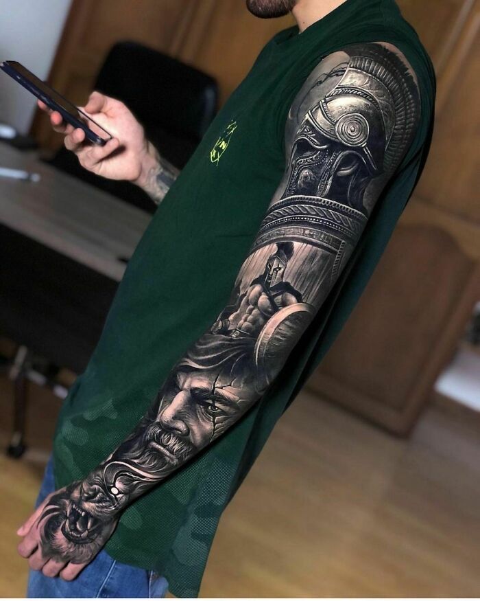 Person with detailed sleeve tattoo featuring intricate warrior design, holding a smartphone. Crazy tattoos showcase.
