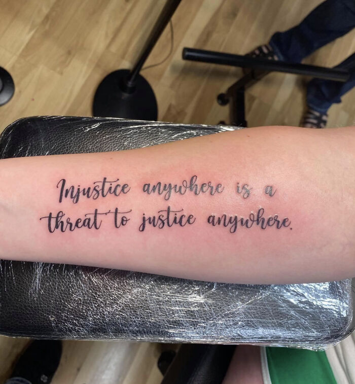 Tattoo on forearm reading "Injustice anywhere is a threat to justice anywhere," possibly considered a red flag by some.