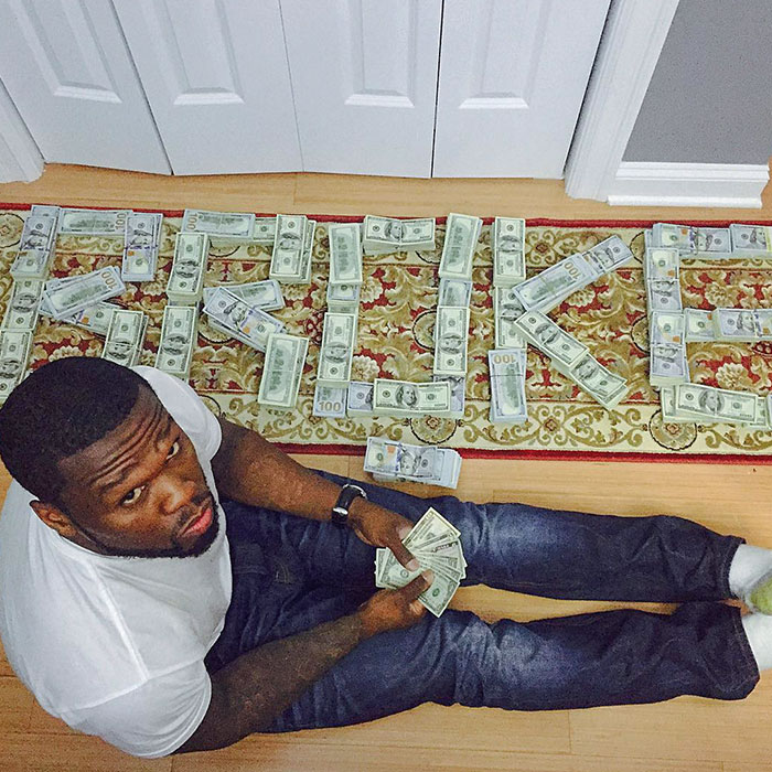 Celebrity sitting with dollar bills spelling "Broke," illustrating flaunted wealth.