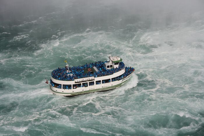 Tour boat filled with passengers wearing blue raincoats navigating rough ocean waters surrounded by mist and waves. - 2