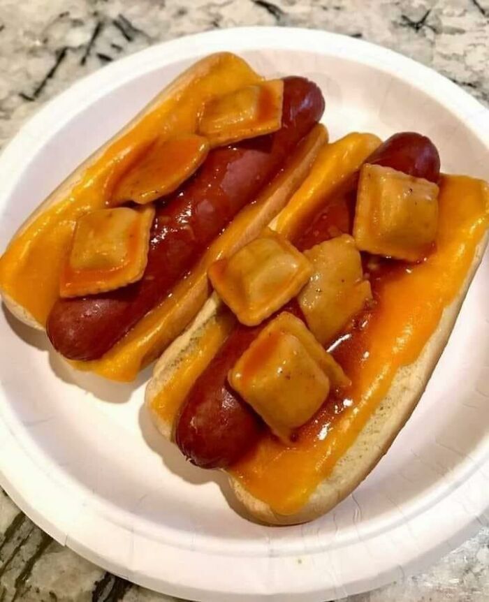 Hot dogs with melted cheddar cheese and ravioli pieces in sauce on a white paper plate, food with threatening auras.