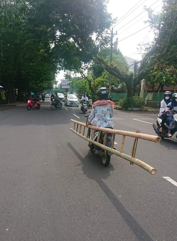 Motorcyclist carrying an oversized wooden ladder dangerously on a busy street, illustrating examples of bad drivers.