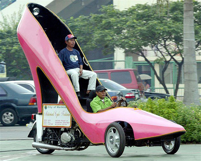 Two men driving a pink high-heel shaped car, an unusual example of bad drivers and unique vehicles on the road.
