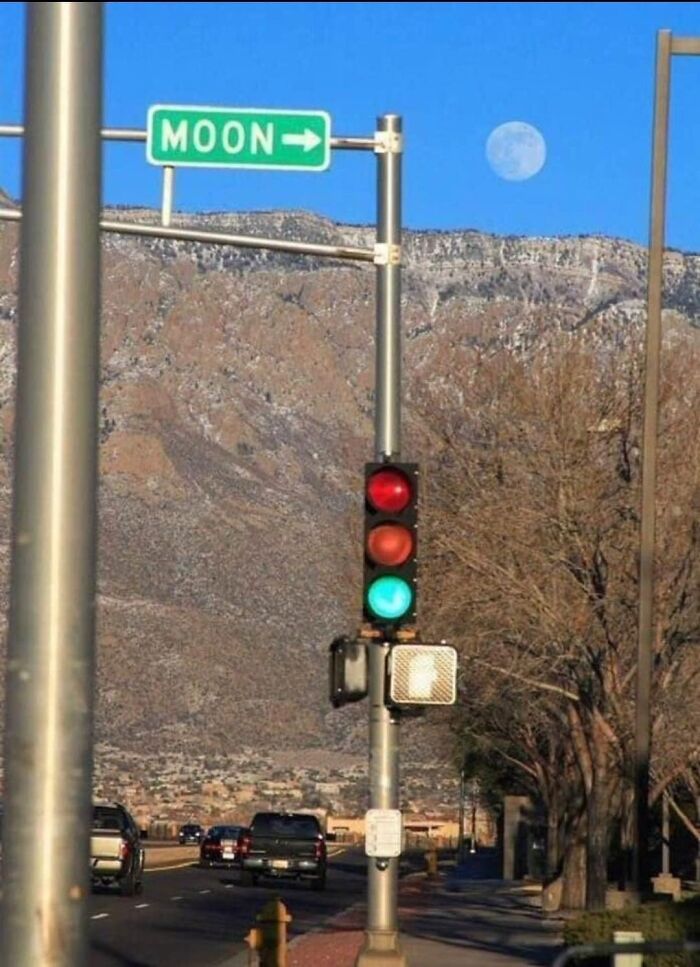 Traffic light showing green while cars stop below a road sign pointing to the moon, highlighting bad drivers examples.