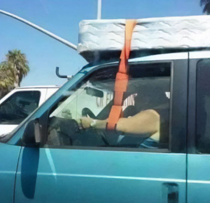 Driver securing mattress on car roof with an orange strap, illustrating examples of bad drivers from a popular Facebook group.