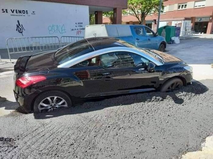 Black car stuck in fresh asphalt on city street, showcasing an example of bad drivers shared in a popular Facebook group.