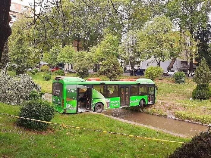 Green hybrid bus stuck in shallow creek with doors open, illustrating examples of bad drivers in a public park area.