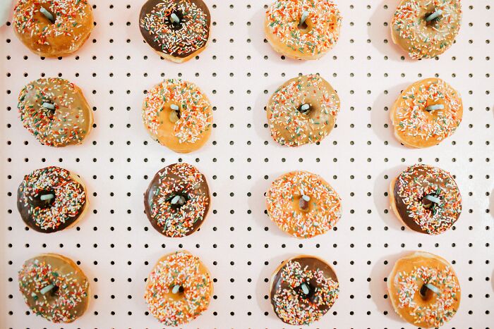Donut wall with colorful sprinkled donuts arranged on a pegboard, showcasing a unique wedding experience idea.