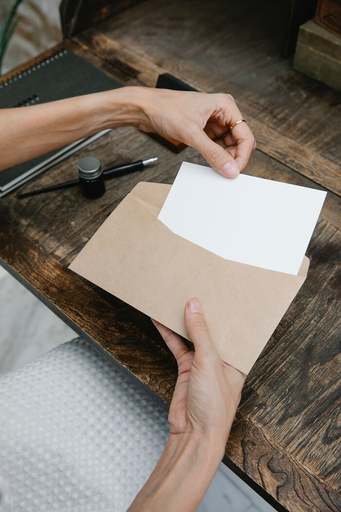 Hands placing a blank card into a brown envelope on a wooden table, representing what was better in the past concept.