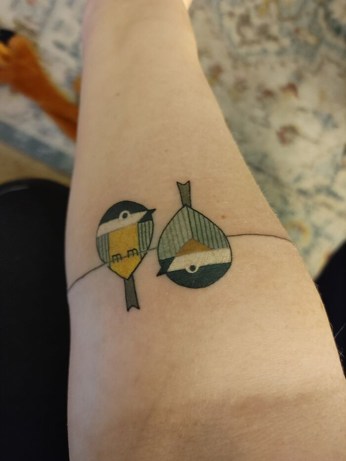 Minimalist bird tattoo on forearm with geometric patterns in yellow, green, and white.