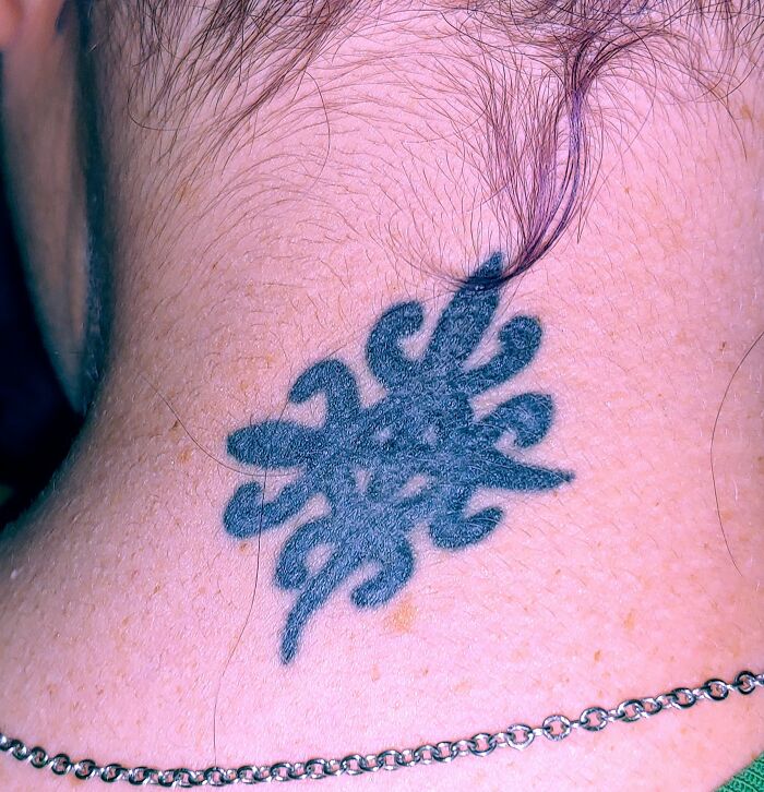 A black tribal tattoo design on the neck, close-up view.