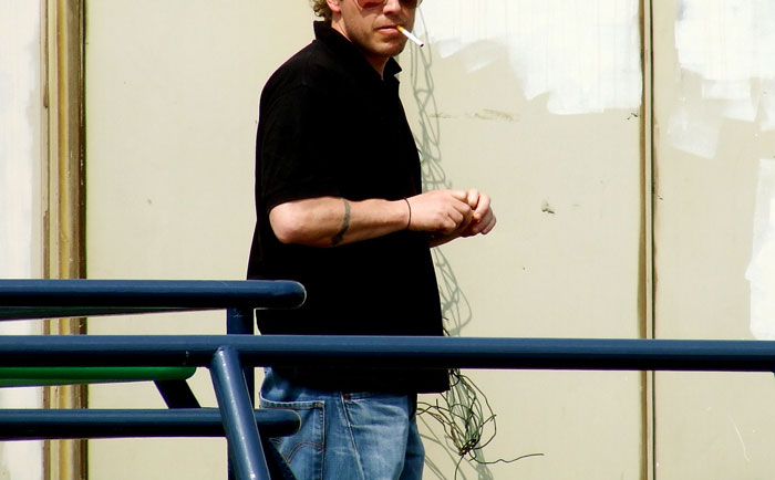 Man wearing sunglasses and black shirt smoking a cigarette outdoors, illustrating things guys should never say to partners.