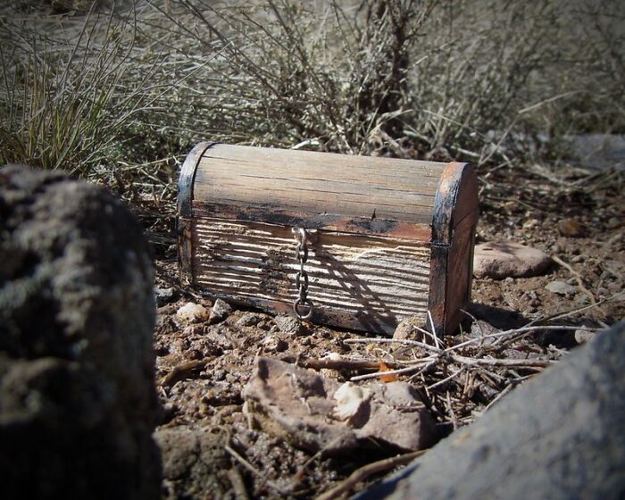 Weathered wooden chest with metal latch resting on dry ground surrounded by sparse vegetation and rocks, illustrating things guys should never say.