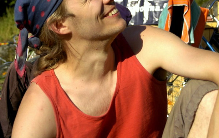 Young man in a red tank top and headscarf smiling outdoors, illustrating things guys should never say to partners.